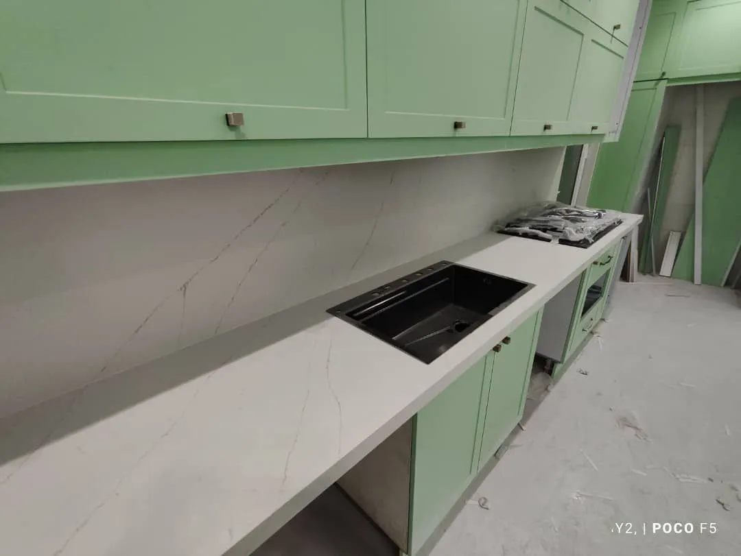 تضاد شیک: سینک مشکی توکار بر روی صفحه کوارتز سفید رگهدار، نصب شده بر کابینتهای نعناعی.